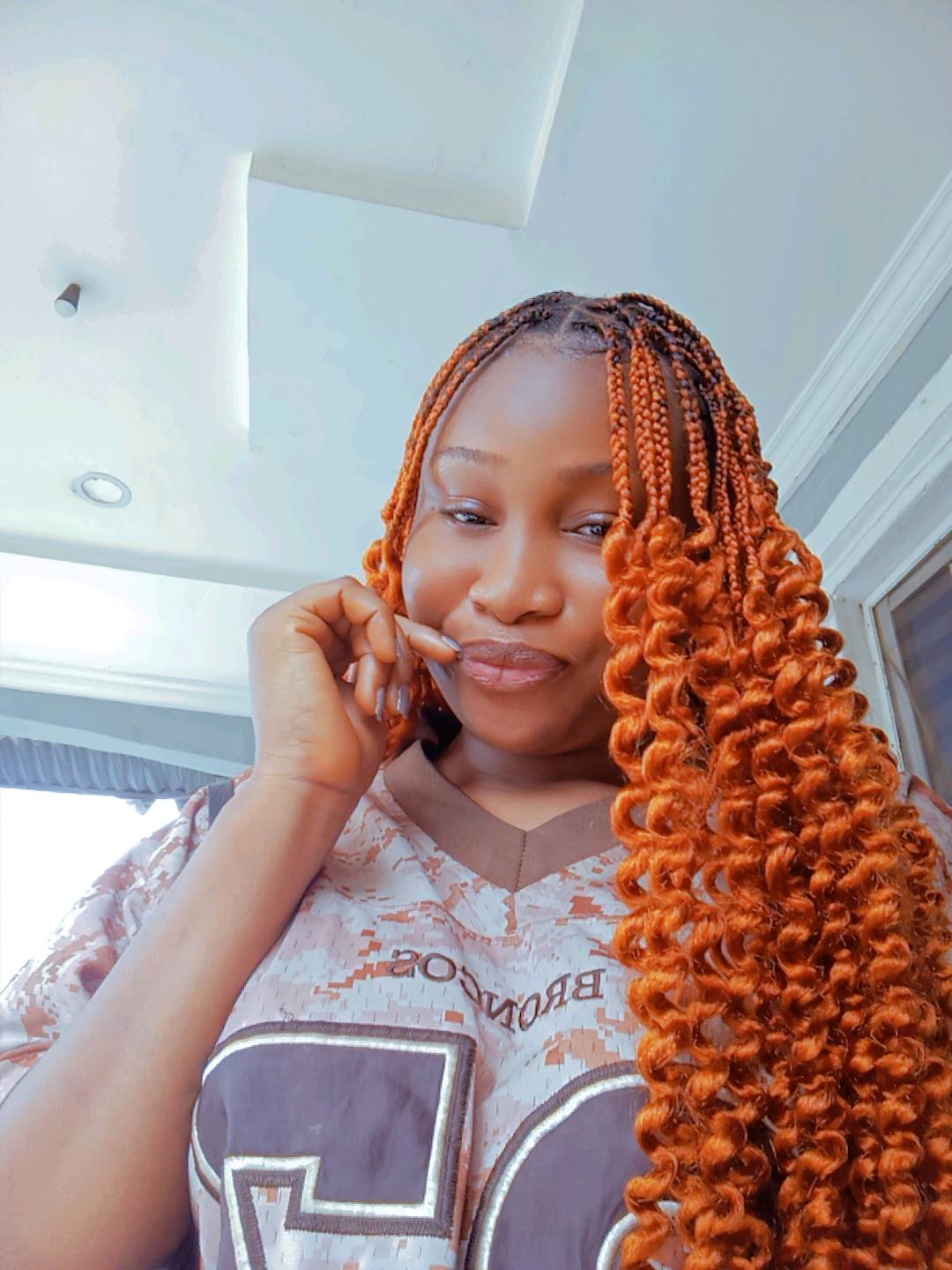 A woman from Nigeria with long copper braids, relaxed at home