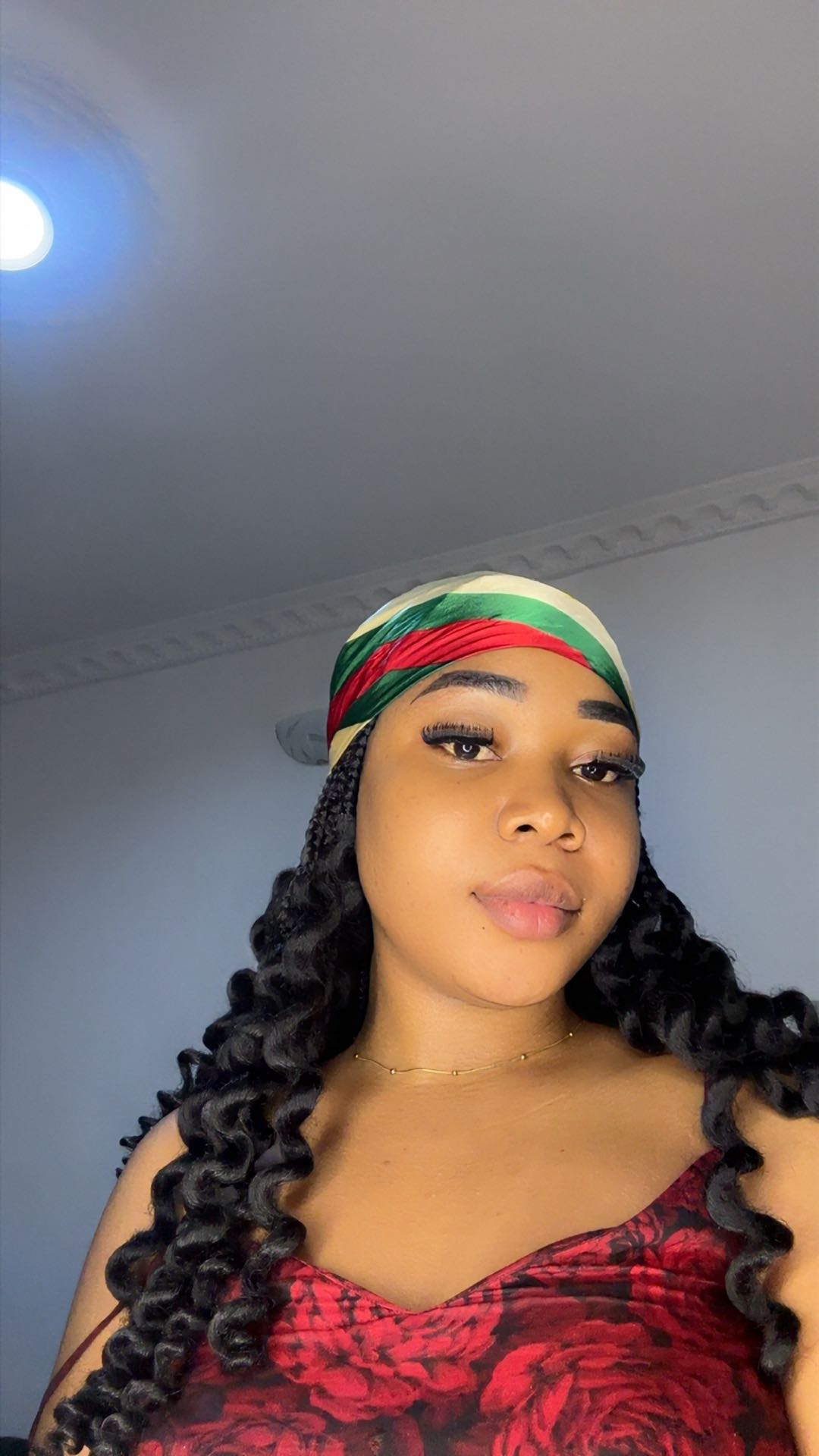 A woman from Nigeria in a red floral top and headwrap, lit like a girl about to go live