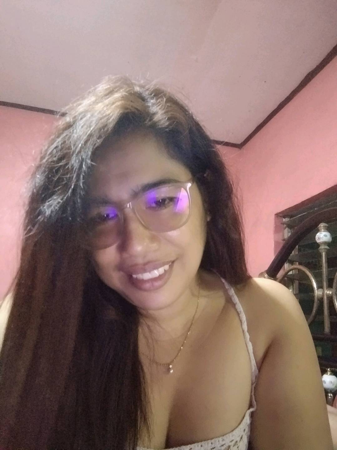 A woman from the Philippines in glasses smiling in her room