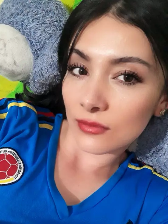 A woman from Colombia in a blue football shirt looking straight into the lens, ready to video chat