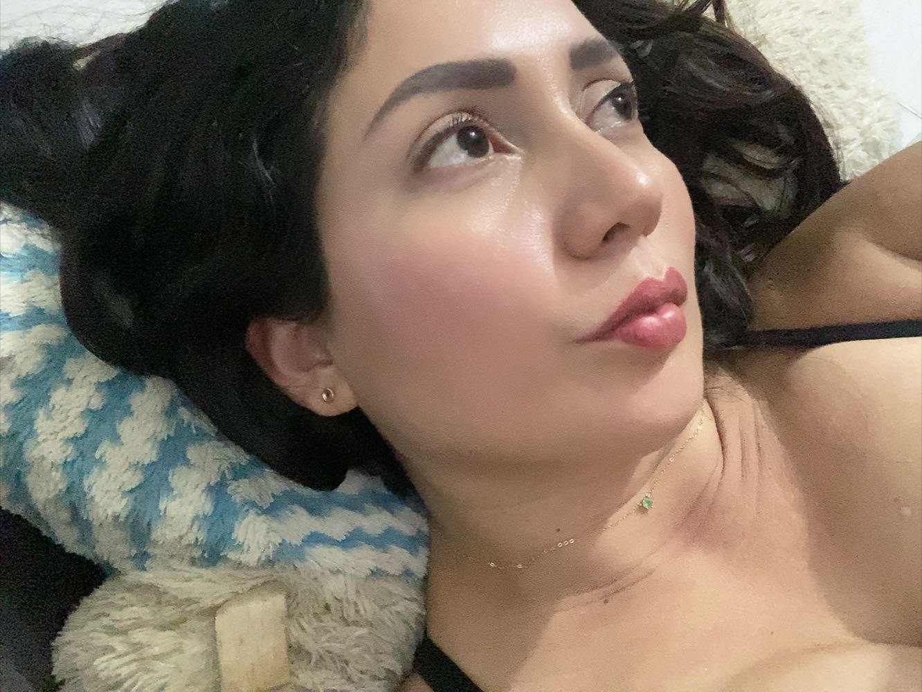 A woman from Colombia resting on a pillow at home, the kind of cam chat that starts on a quiet evening