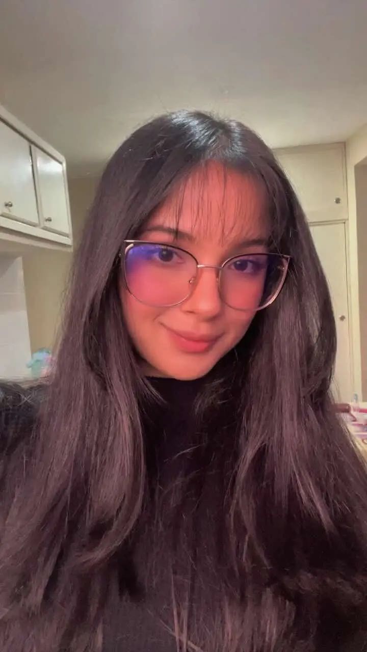 A woman from Venezuela in round glasses smiling at her camera
